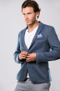 Fashion portrait of a handsome man with trendy hairstyle in a stylish jacket on light background