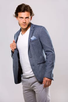 Fashion portrait of a handsome man with trendy hairstyle in a stylish jacket on light background