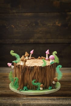 Enchanted forest woodland themed fondant cake with a tree trunk, ferns, mushrooms and leaves on wooden background with copyspace
