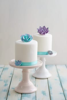 Two white mini wedding cakes covererd with fondant with gum paste succulents on cake stands