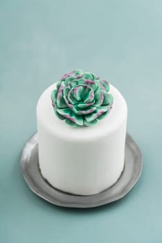 White mini wedding cake covered with fondant with gum paste succulent on a pewter plate