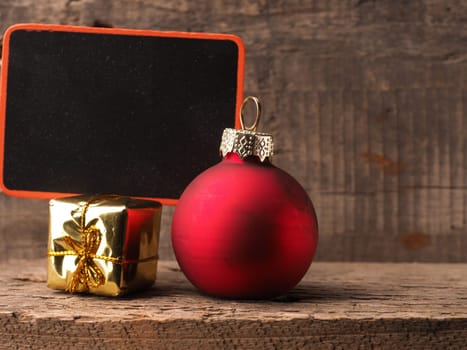 Small chalkboartd with an old Christmas bauble and gift box on a rustic wooden background