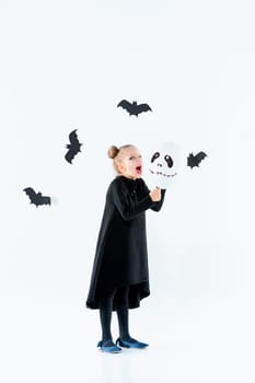 Little girl witch in black long dress and magical accessories. Halloween, the studio evening.