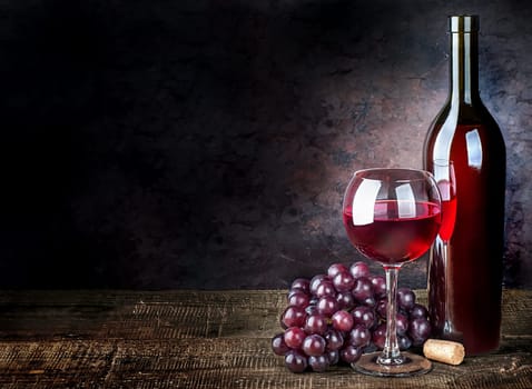 Glass of red wine with grapes and bottle on a wooden table