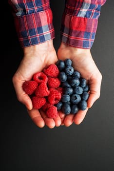 Woman hands holding fresh berries, raspberries and blueberries on black background