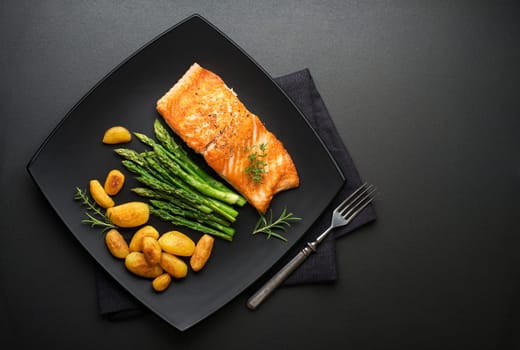 Roasted salmon fillet with asparagus and potatoes on black background