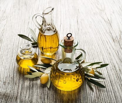 Olive oil in bottles with branch on the wooden background