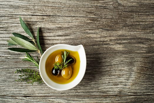 Olive oil with fresh herbs on wooden background
