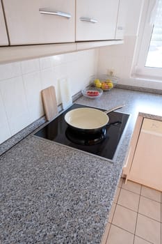 Fitted kitchen with ceramic hob and frying pan in portrait format