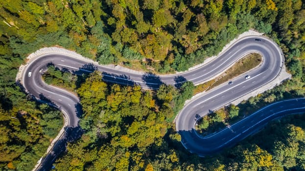 Curved road trough the forest. Pass in Transylvania, Romania. Aerial view from a drone.