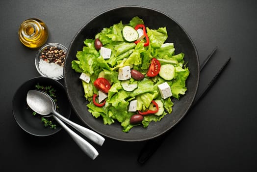 Green salad with cheese and fresh vegetables on a black background. Greek salad.