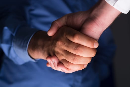 Low angle view of two businessmen hands shaking over dark gray background and light source at bottom side