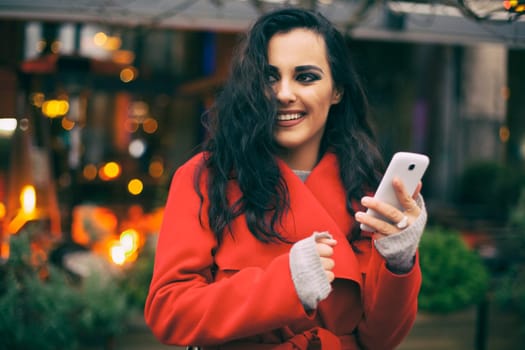 Traveling Smiling Woman in Red Coat hold Mobile Phone, smartphone In City, Urban Space, noise on image