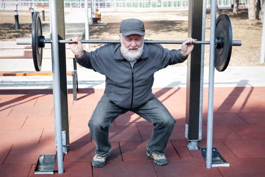 An old man lifting weights in the fitness park.