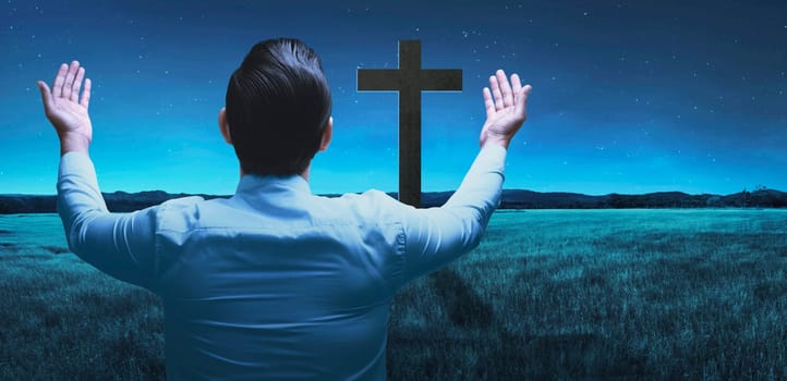 Back view of man raising hand while praying to god over night background