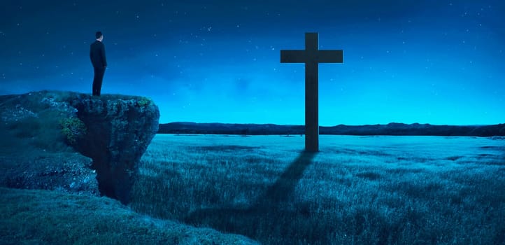 Man standing on the top of the cliff looking to the cross. Religion concept