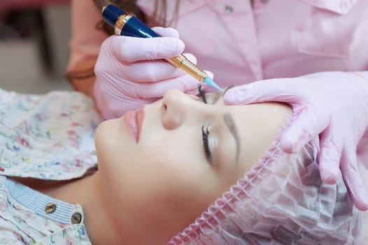 A young woman lies and gets a make-up of her eyebrows in a beauty salon. The use of permanent makeup on the eyebrows. The master works with the eyebrows. Semi-permanent makeup.