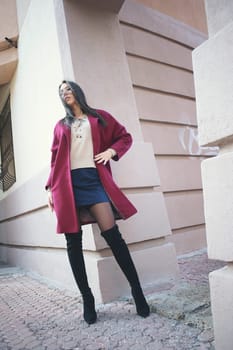 young beautiful stylish woman walking in burgundy coat, street style, spring summer trend, dark skirt, beige jacket, flirty.