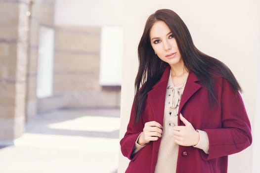 young beautiful stylish woman walking in burgundy coat, street style, spring summer trend, dark skirt, beige jacket, flirty.