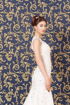 Beautiful young bride with makeup and fancy hairstyle in fancy dress sitting on bed.