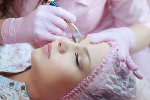 A young woman lies and gets a make-up of her eyebrows in a beauty salon. The use of permanent makeup on the eyebrows. The master works with the eyebrows. Semi-permanent makeup.