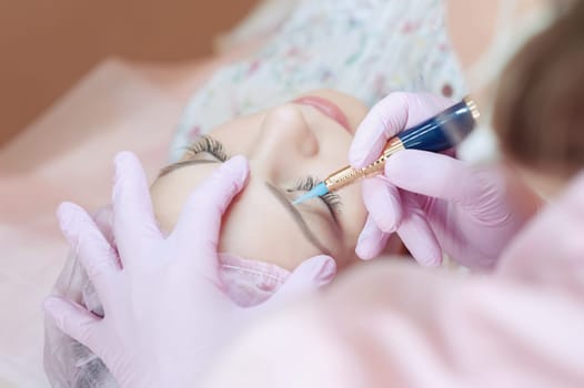 A young woman lies and gets a make-up of her eyebrows in a beauty salon. The use of permanent makeup on the eyebrows. The master works with the eyebrows. Semi-permanent makeup.