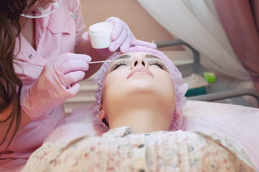 A young woman lies and gets a make-up of her eyebrows in a beauty salon. The use of permanent makeup on the eyebrows. The master works with the eyebrows. Semi-permanent makeup.