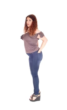 A young woman standing in jeans and sweater in profile, holding her.hand in pocket, with curly hair, isolated for white background.
