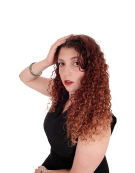 A young woman in a black dress holding one hand on her head, with.curly long brunette hair, isolated for white background..