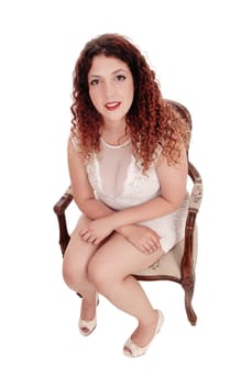 A young full figured woman in a beige lace dress sitting in an old.armchair, looking up into the camera, isolated for white background.