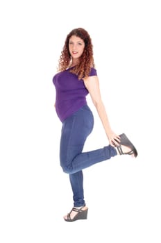 A young woman standing in jeans and sweater in profile, holding her.leg up, with curly hair, isolated for white background.