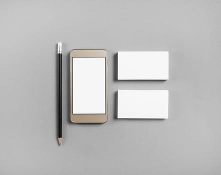 Mockup of blank business cards, pencil and cellphone with blank screen at gray paper background. Top view.
