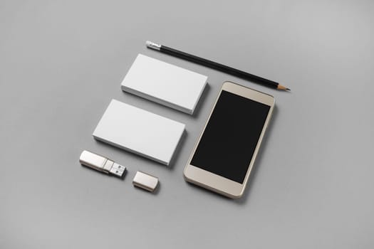 Gadgets and stationery. Mockup of blank business cards, pencil, usb flash drive and cellphone with blank screen on gray paper background.
