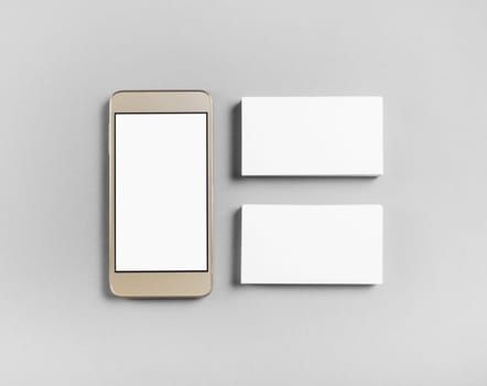 Blank business cards and smartphone on gray paper background. Objects for placing your design. Top view.
