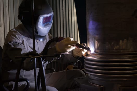 Welder with protective mask welding metal and sparks.