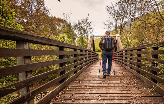 Mature man are hiking in the mountains, walking on a wooden bridge