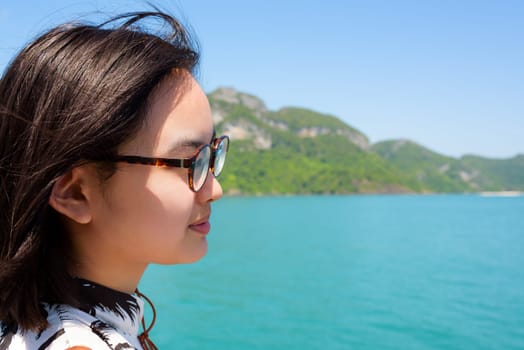 Cute young woman with eyeglasses smiling happily on the boat while cruising the beautiful natural of the blue sea and sky in summer at Mu Ko Ang Thong National Park, Surat Thani, Thailand
