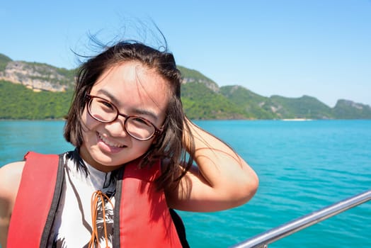 Cute young woman with eyeglasses smiling happily on the boat while cruising the beautiful natural of the blue sea and sky in summer at Mu Ko Ang Thong National Park, Surat Thani, Thailand