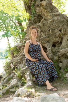 a beautiful pregnant woman sitting under a tree
