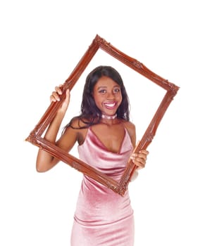 A gorgeous African woman holding up a picture frame and looking.trough, in a pink dress and smiling, isolated for white background.