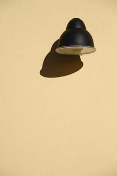 The close-up of a wall lamp that casts a shadow on a plaster façade.