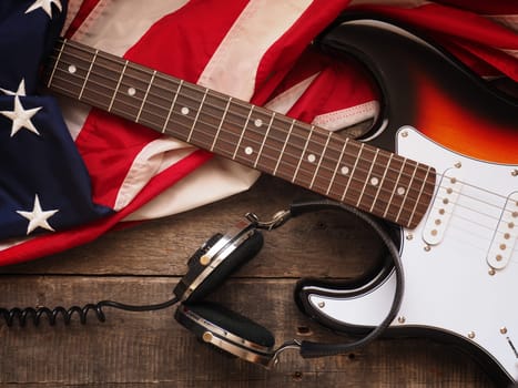 Old used rock guitar with headphones and the American flag on rustic wood, music or sound concept background