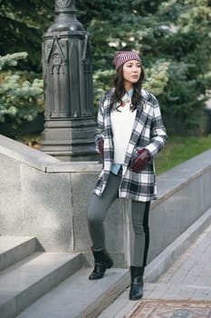 Young beautiful stylish woman, wearing a coat in a white and black cage, white jacket, gray trousers, black boots. Street style, spring and autumn trend, a flirty look.