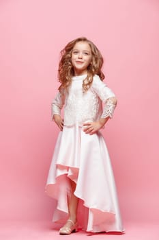 Full length of beautiful little girl in long dress standing and posing over pink background