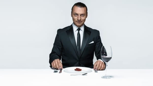 Portrait of a young man in image of maniak with knife, fork and and a piece of raw meat on a plate. Man in suit. The image in the style of Halloween