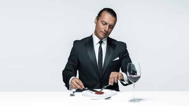 Portrait of a young man in image of maniak with knife, fork and and a piece of raw meat on a plate. Man in suit. The image in the style of Halloween