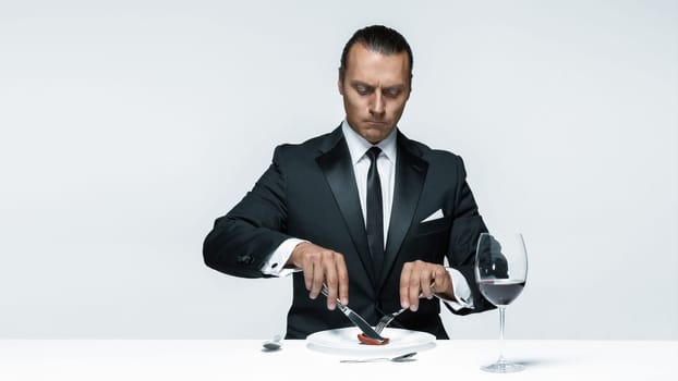 Portrait of a young man in image of maniak with knife, fork and and a piece of raw meat on a plate. Man in suit. The image in the style of Halloween