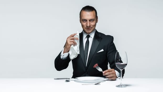 Portrait of a young man in image of maniak with knife, fork and and a piece of raw meat on a plate. Man in suit. The image in the style of Halloween