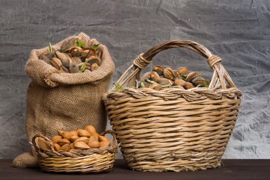Almonds over a rustic wooden board. Rustic sack and basket. Nutcracker and almond oil. Almond flour.