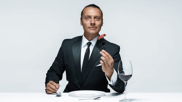 Portrait of a young man in image of maniak with knife, fork and and a piece of raw meat on a plate. Man in suit. The image in the style of Halloween